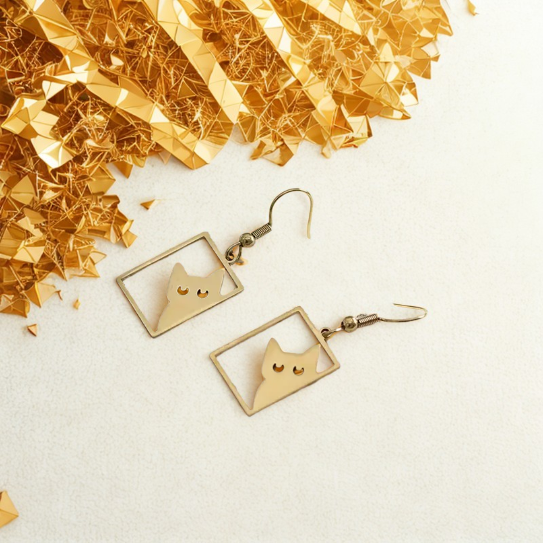 Gold cat earrings with cutout cat faces inside square frames on white background with gold foil decoration